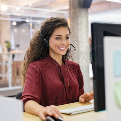 Customer support phone operator working at computer. Happy call center agent working on support hotline in office. Smiling call center agent in conversation with customer over headset.
